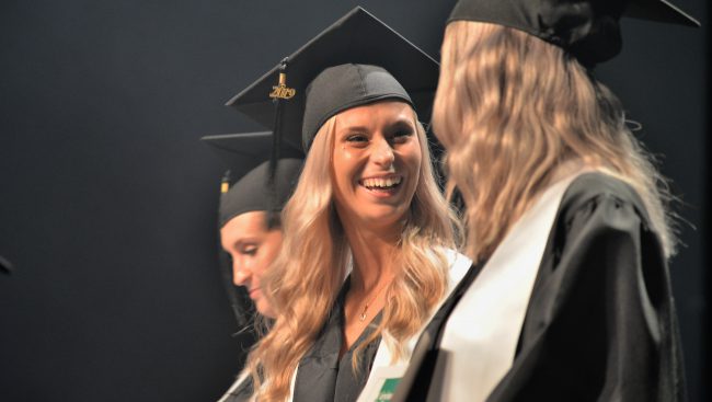 Deux jeunes diplômés se regardent en souriants sur la scène.