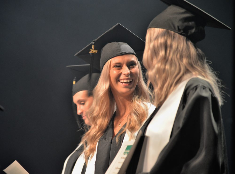 Deux jeunes diplômés se regardent en souriants sur la scène.
