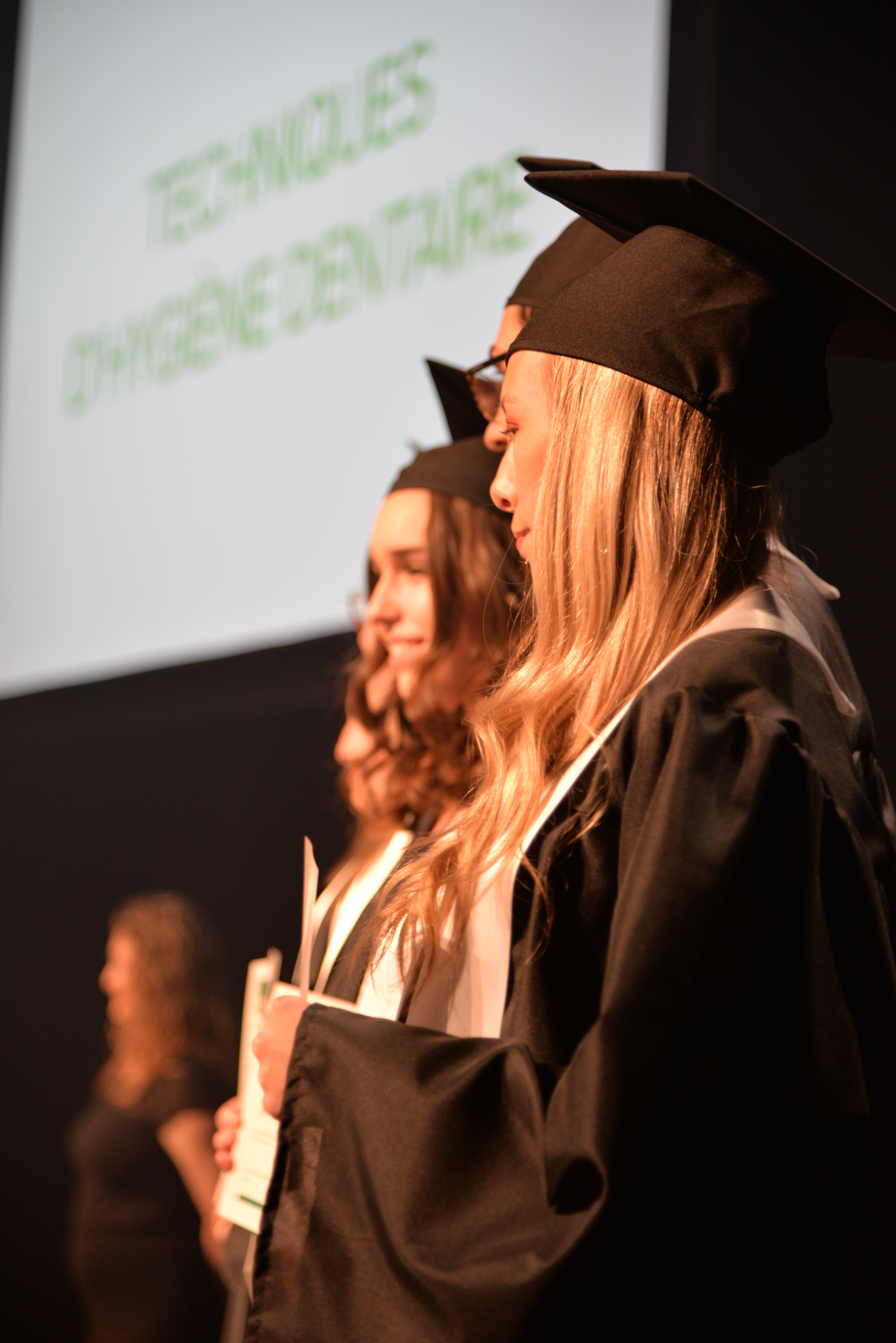 Photo de profil avec deux jeunes finissantes sur scène avec leurs diplômes en main.
